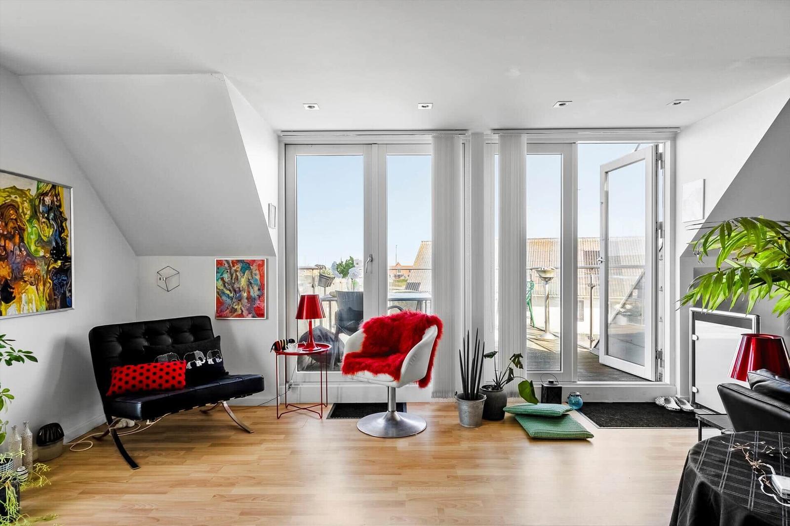 Wohnzimmer mit Blick auf Balkon, rotem Sessel und Kunst an den Wänden.