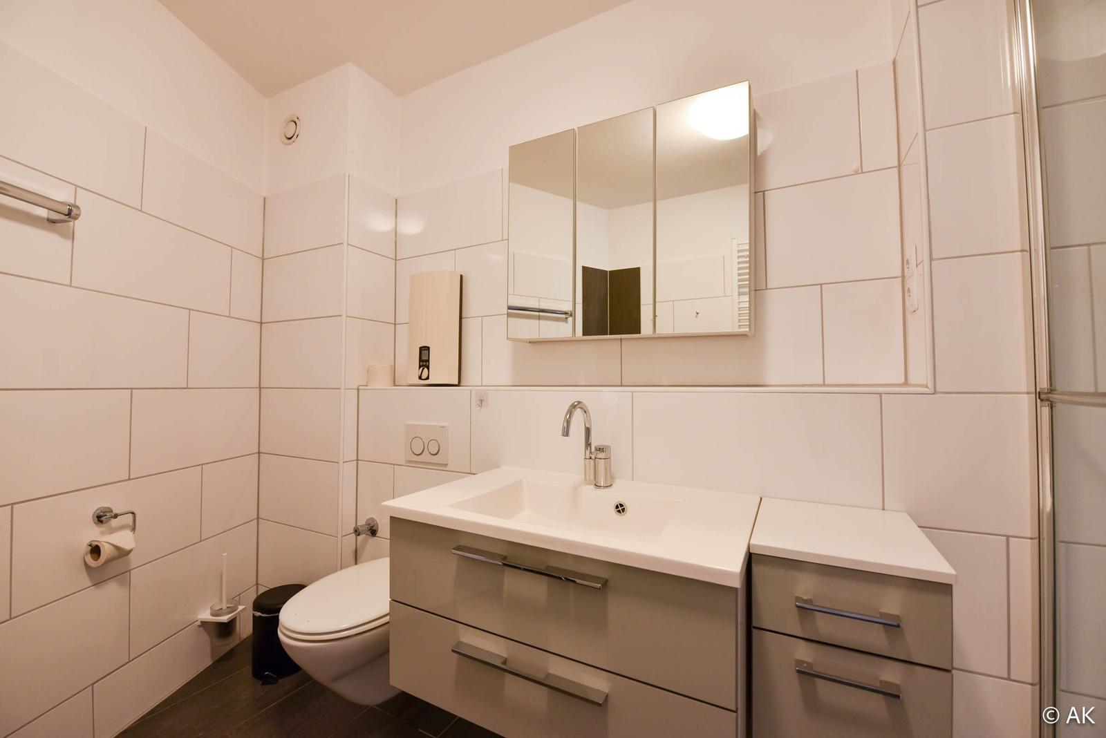 Badezimmer mit Waschbecken, Spiegel, Toilette und Dusche.