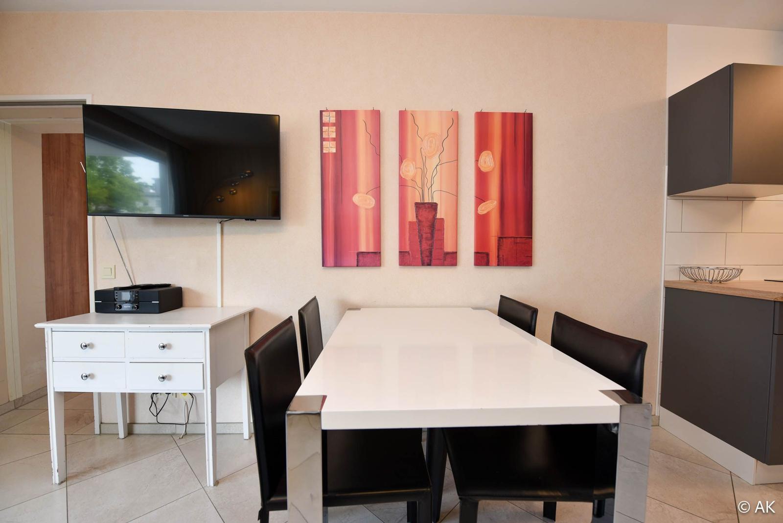 Essbereich mit Tisch, Stühlen, Wandbildern und Fernseher.