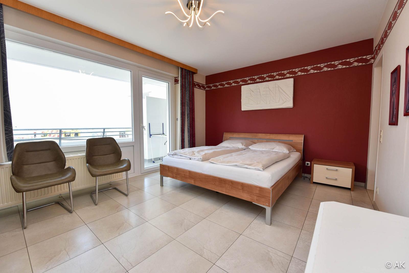 Schlafzimmer mit Doppelbett, zwei Stühlen und Balkontür.