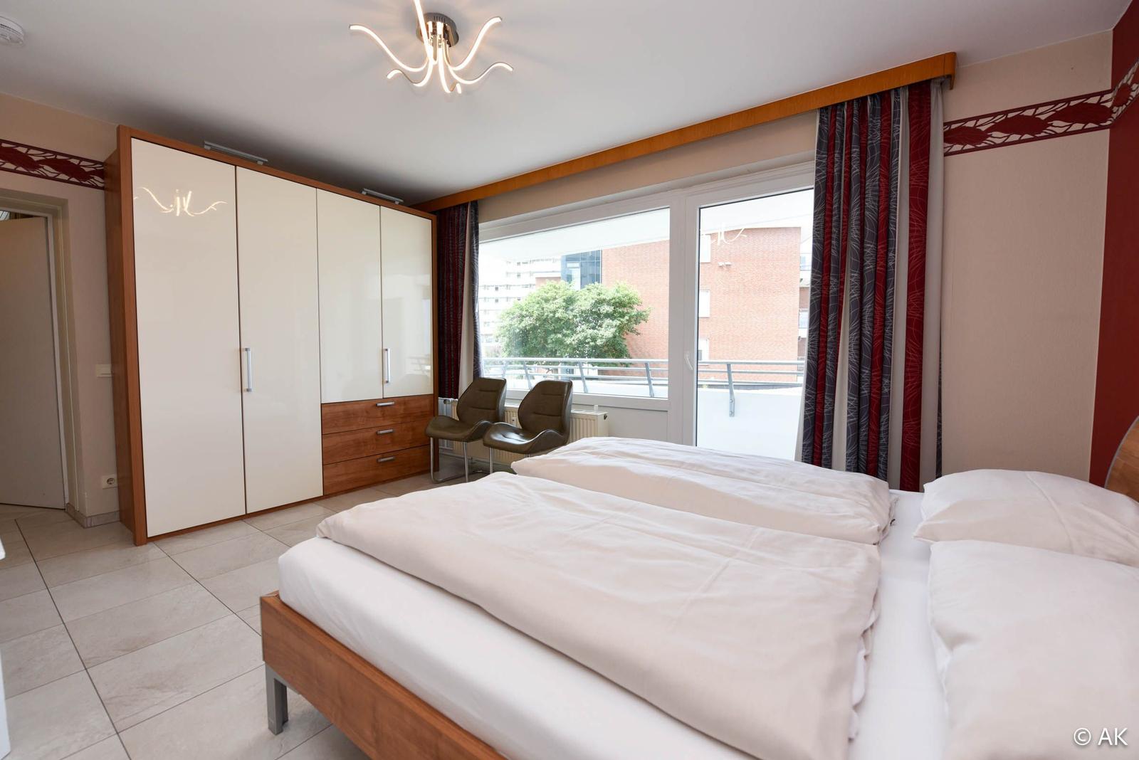 Schlafzimmer mit Doppelbett, Kleiderschrank und Balkonansicht.