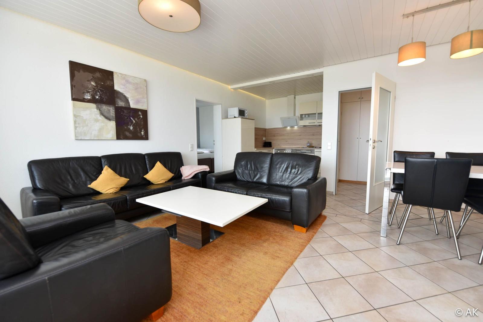 Wohnzimmer mit zwei schwarzen Sofas, weißem Tisch und Essbereich.