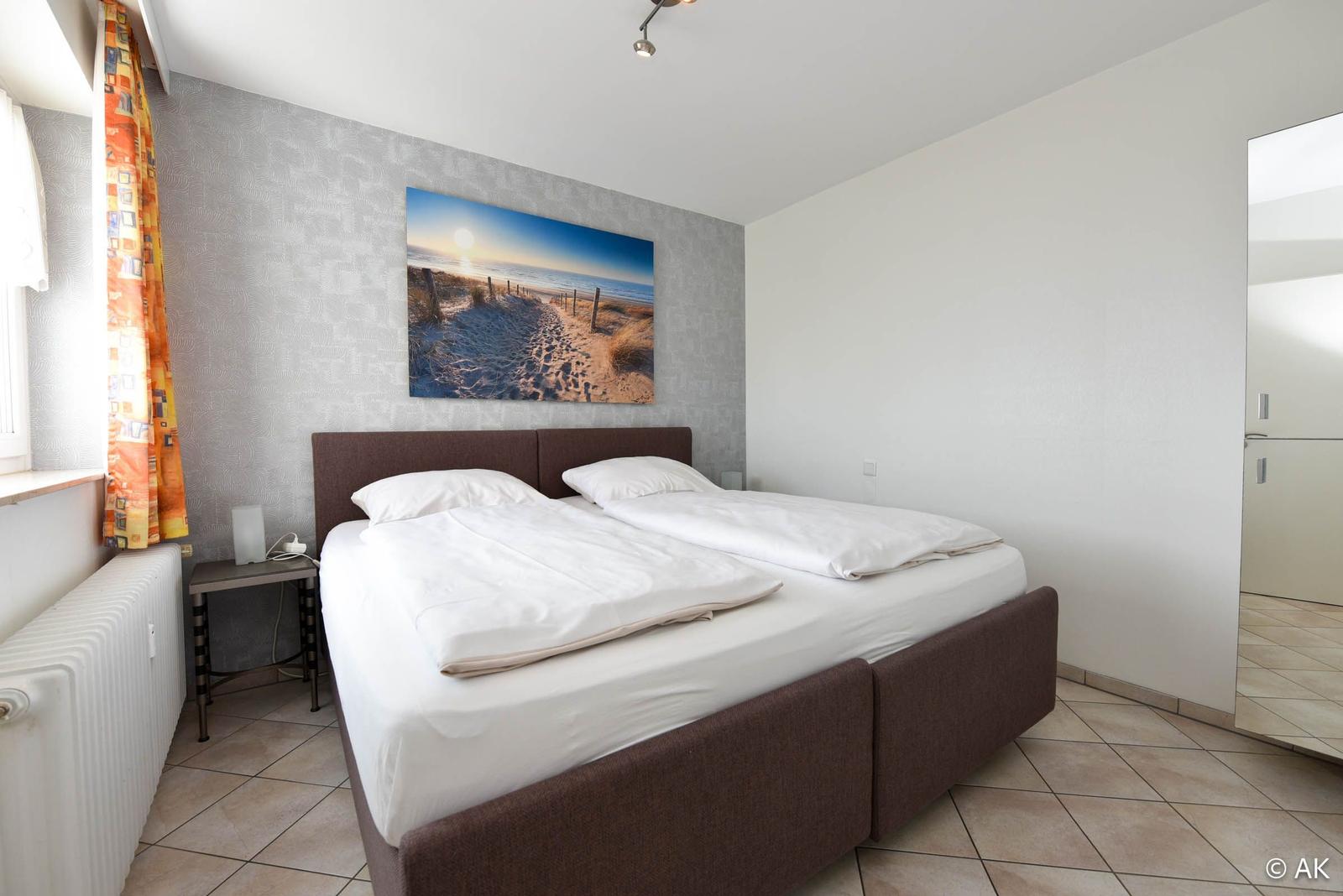 Schlafzimmer mit Doppelbett, Wandbild und Fenster mit Vorhang.