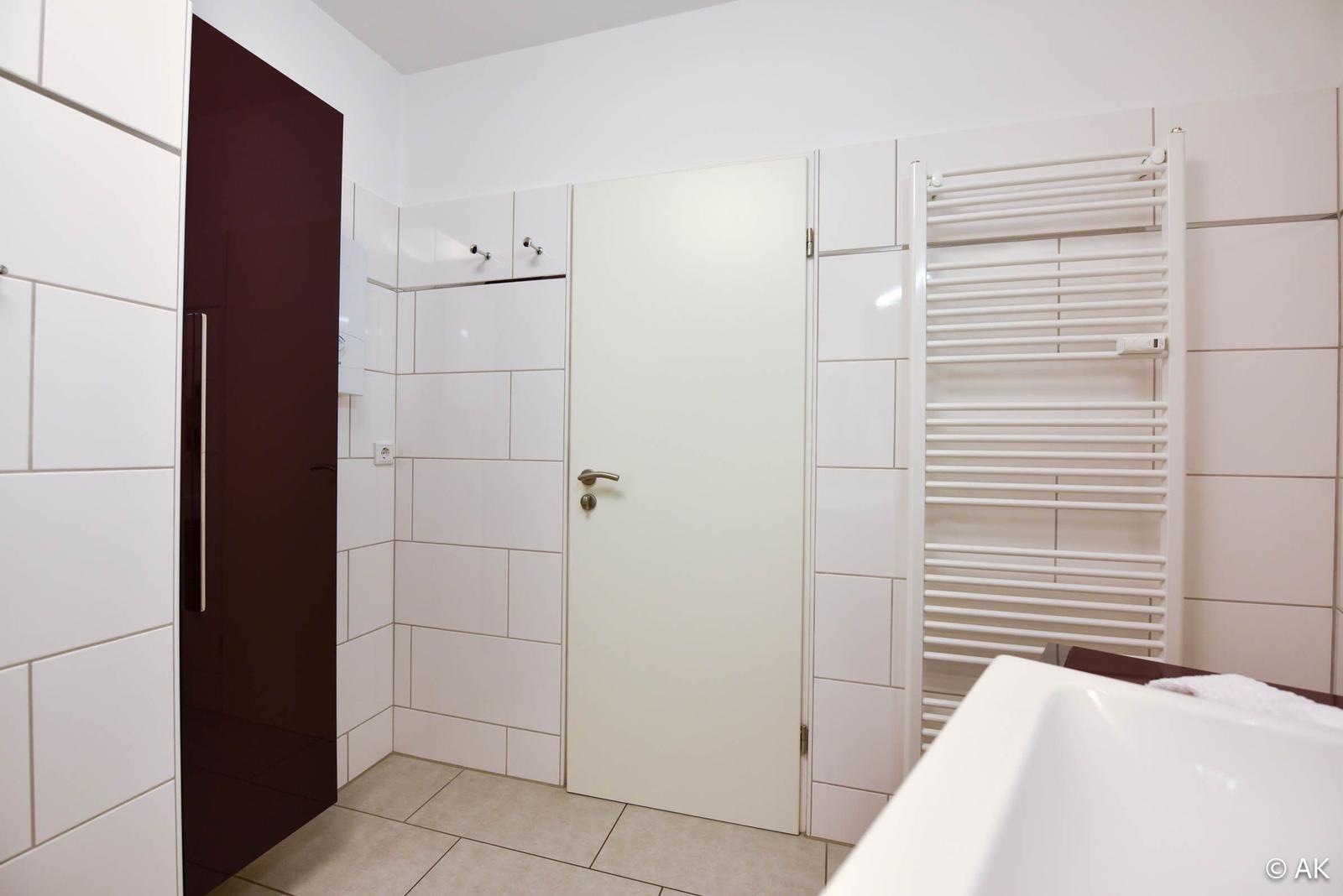 Badezimmer mit Dusche, Heizkörper und weißen Fliesen.