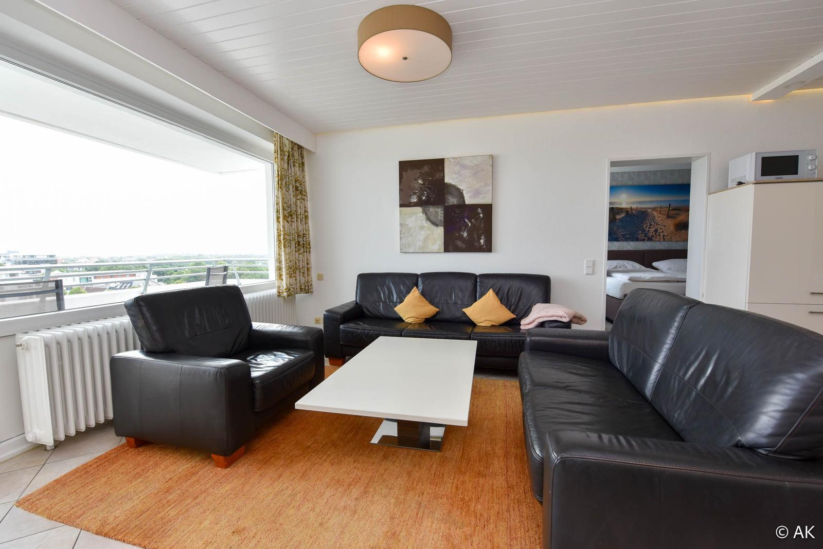Wohnzimmer mit zwei schwarzen Sofas, Tisch und Blick auf Balkon.