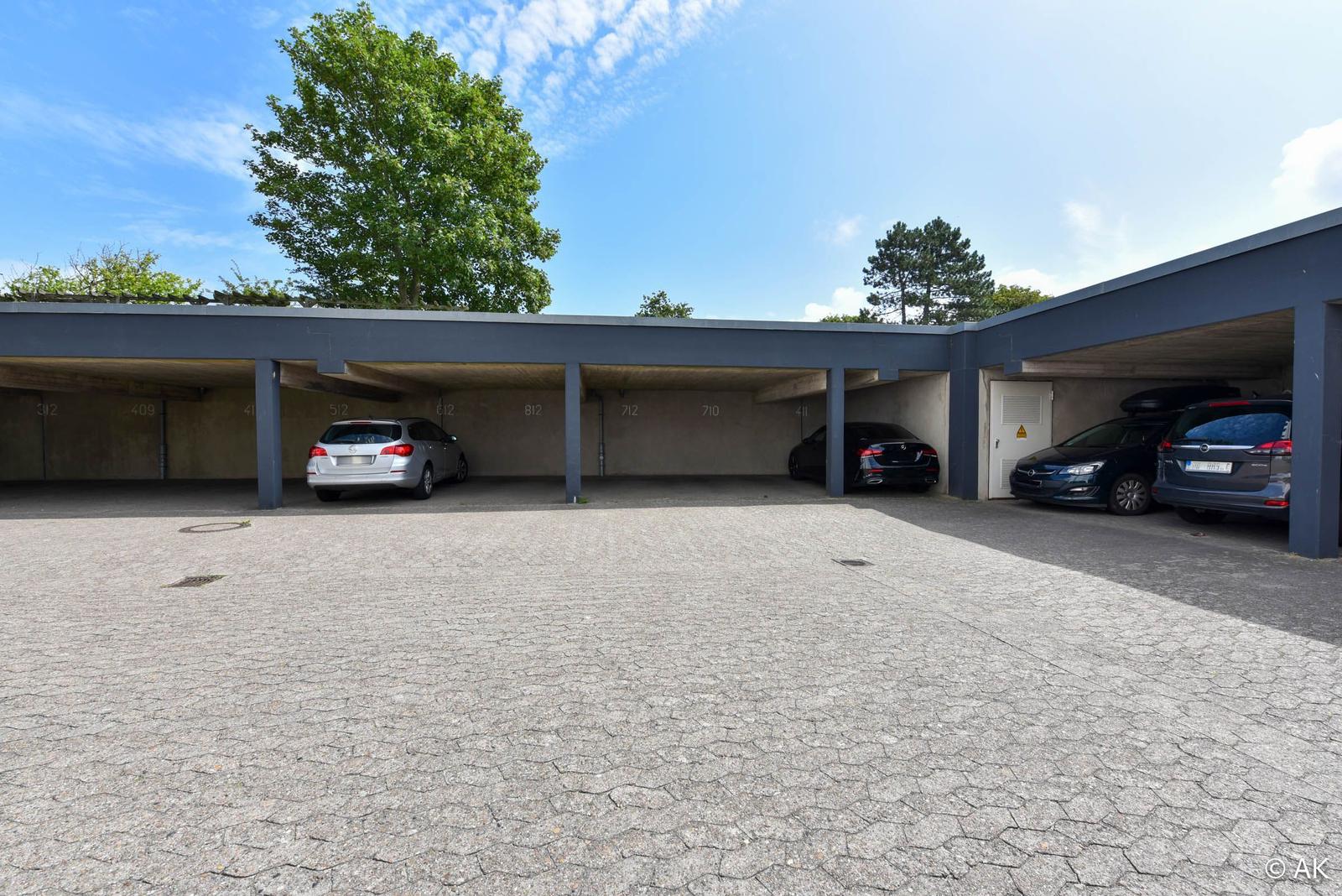 Garage mit mehreren Parkplätzen und gepflastertem Vorplatz unter blauem Himmel.