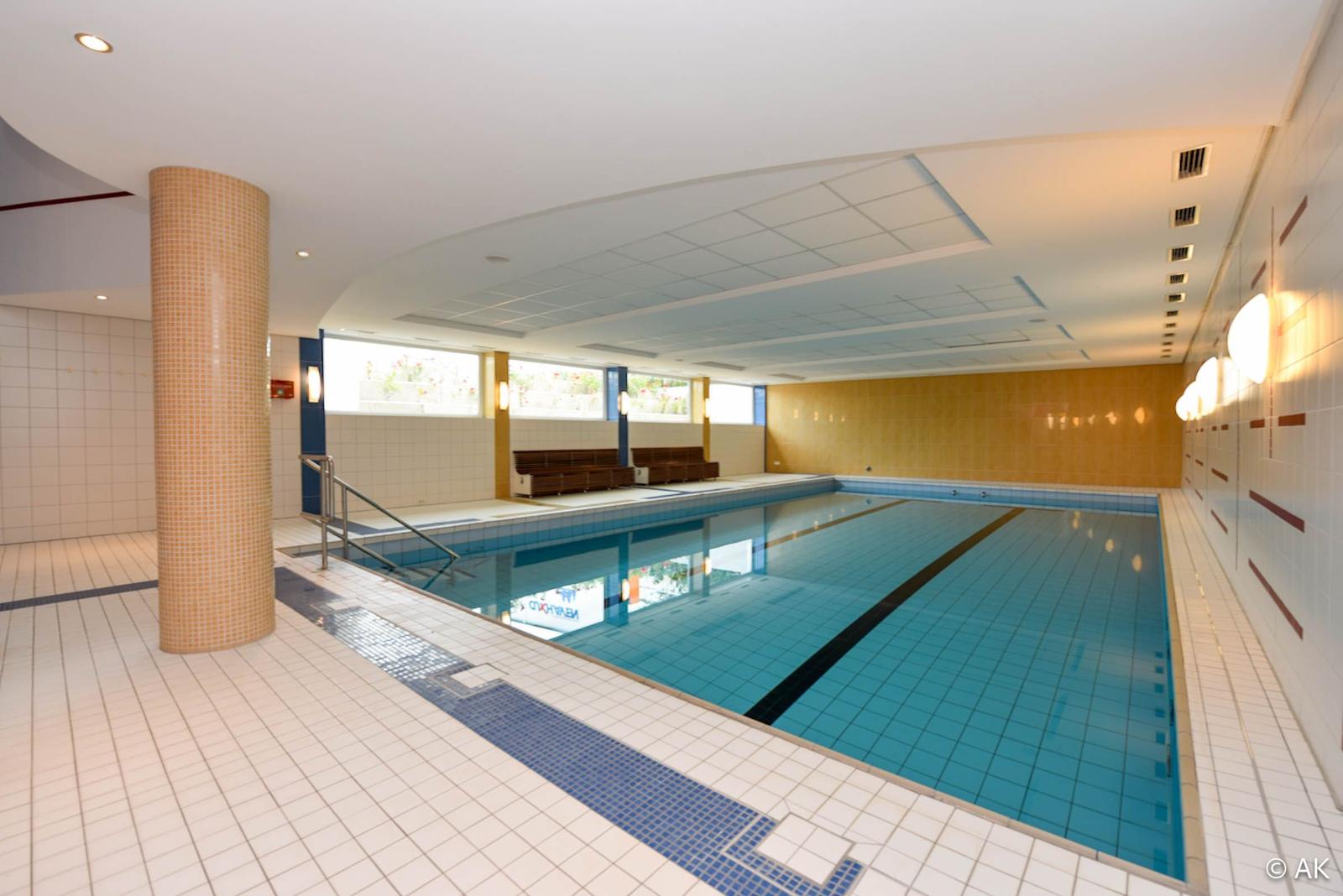 Innenpool mit Treppe, Sitzbänken und beleuchteten Wänden.