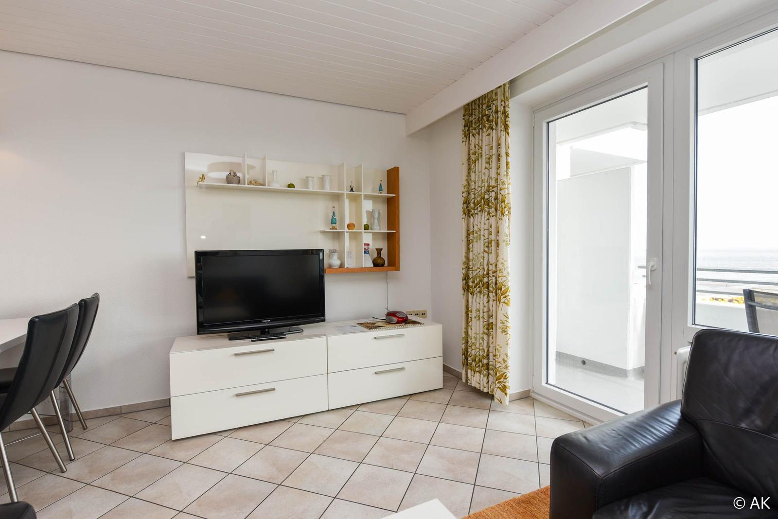 Wohnzimmer mit TV, Schrank und Balkonzugang.