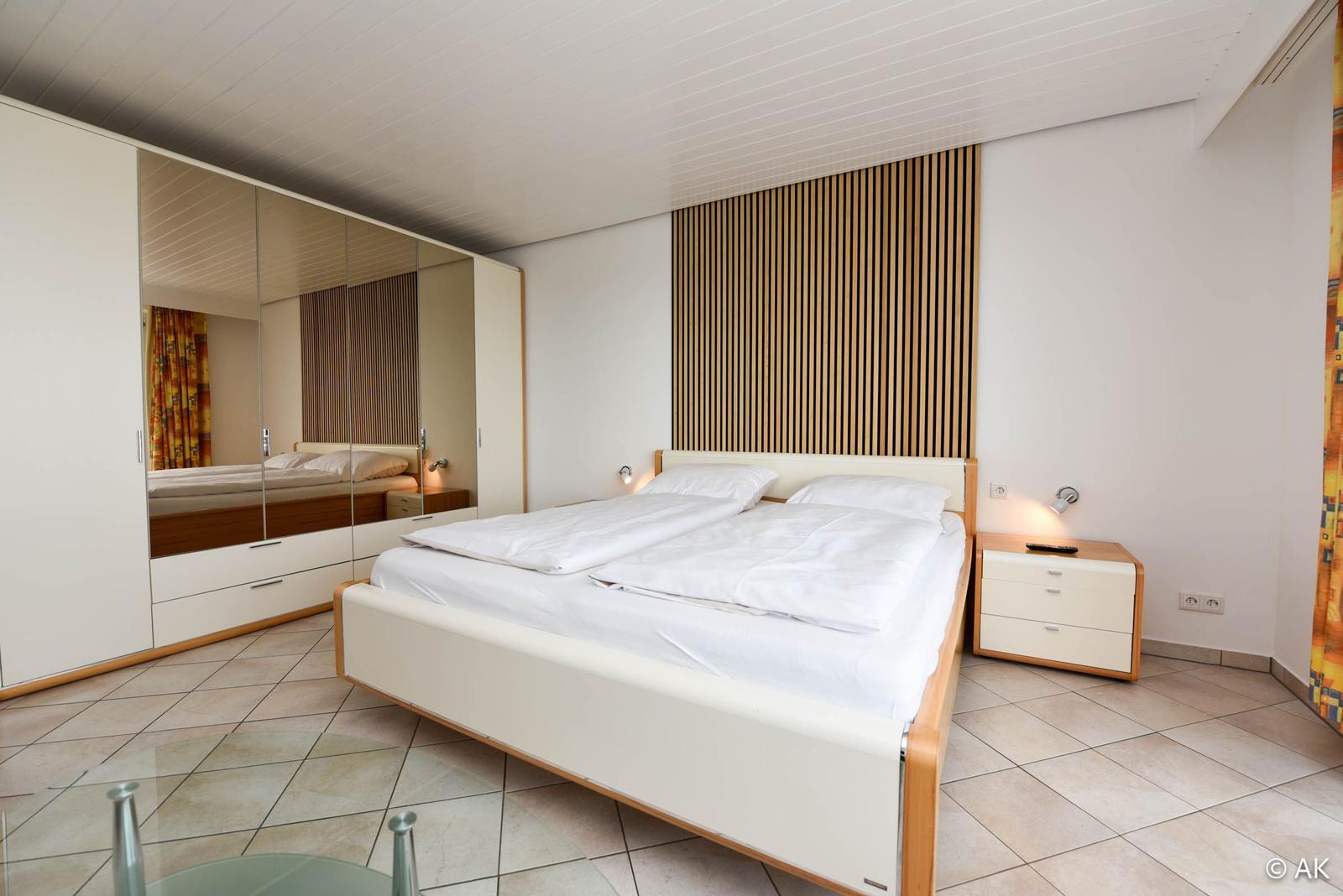 Schlafzimmer mit Doppelbett, Spiegelschrank und Nachttisch.