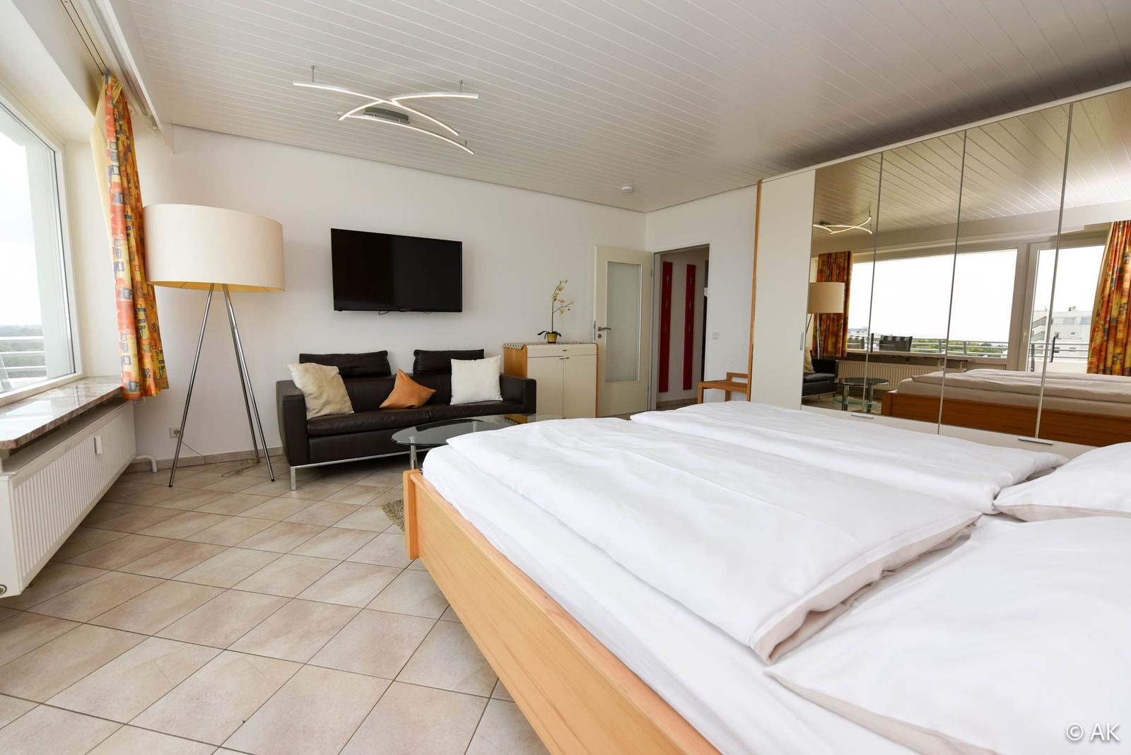 Ein Schlafzimmer mit Bett, Sofa, Fernseher und Spiegelschrank.