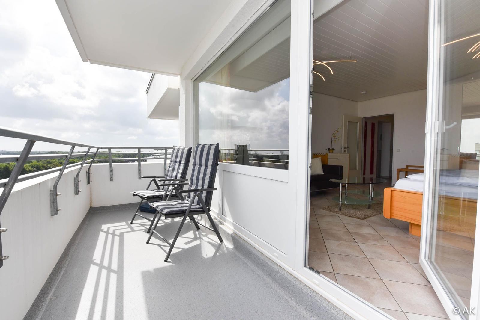 Terrasse mit zwei Stühlen und Blick auf Grünflächen. Durchgehende Glasschiebetüren führen ins Wohnzimmer.