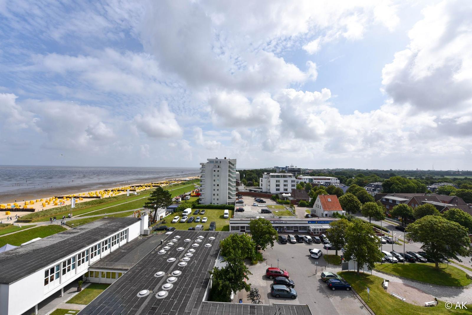 Blick auf Strand, Hotel und Parkplatz mit Bäumen und Autos.