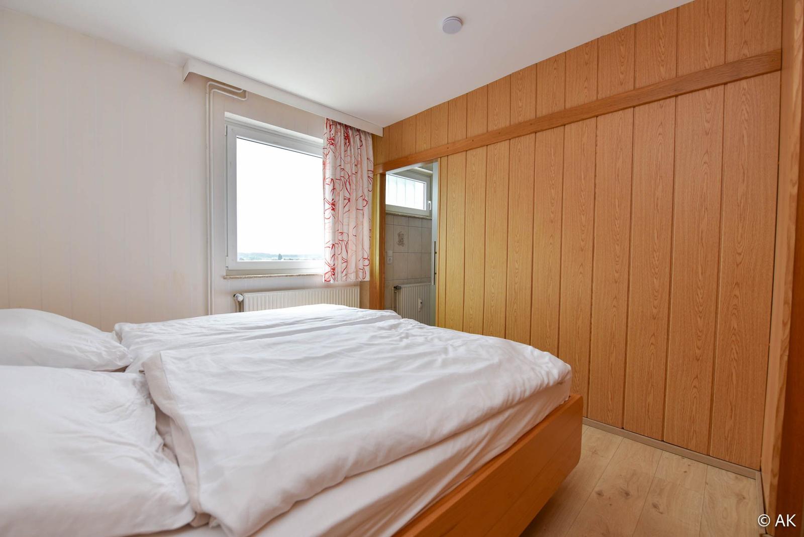 Schlafzimmer mit Doppelbett, Holzwand und Fenster mit Blick.