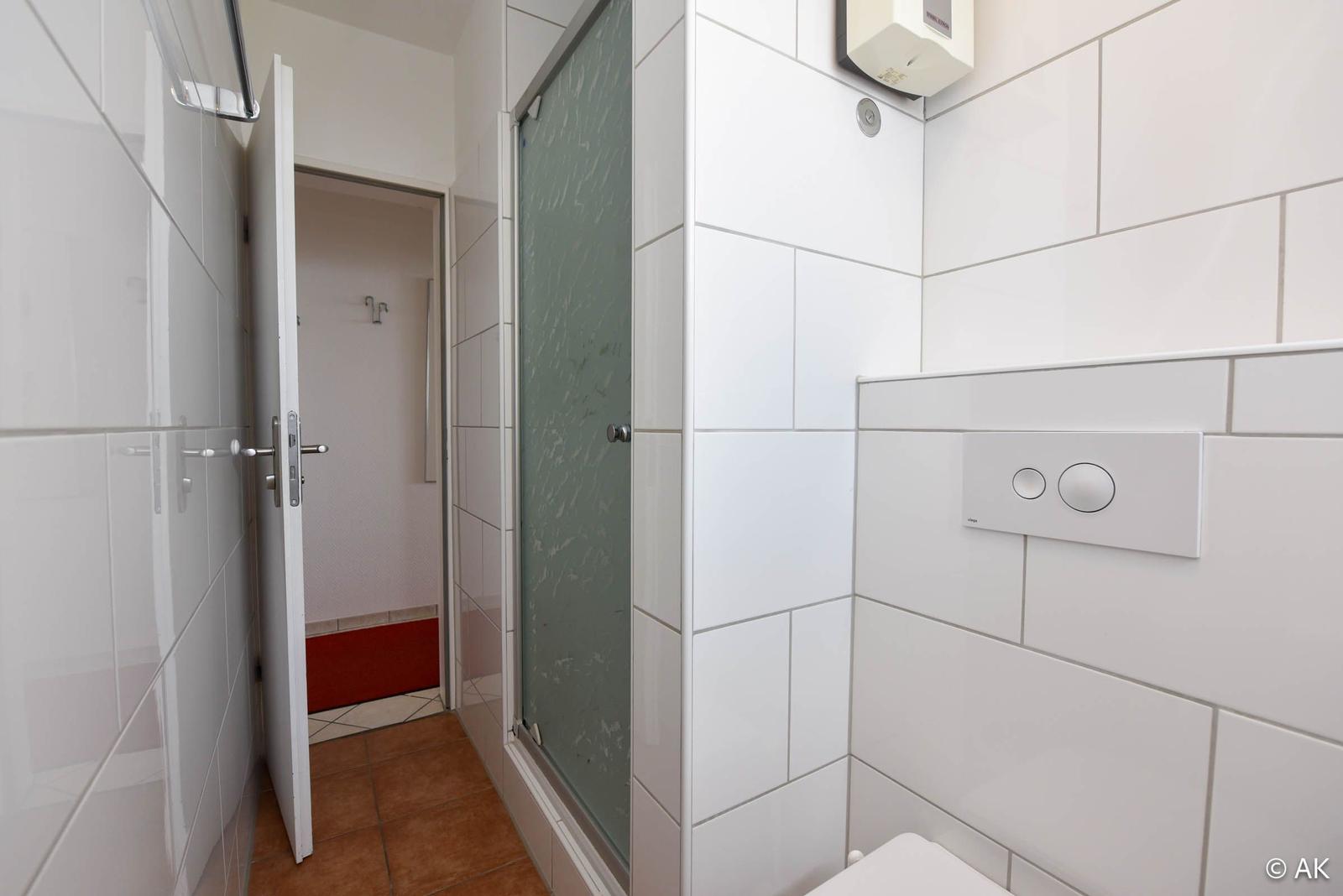 Badezimmer mit Dusche, Toilette und Waschbecken. Tür führt in angrenzenden Raum.