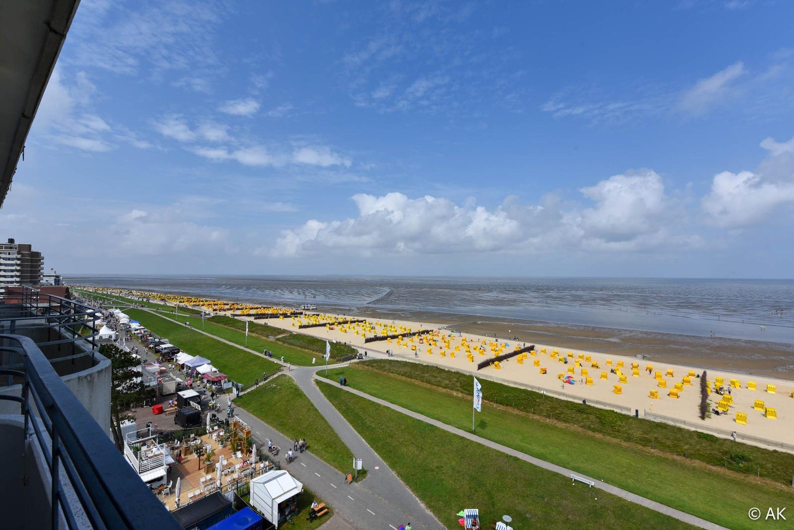 Blick auf Strand mit gelben Strandkörben und Promenade unter blauem Himmel.