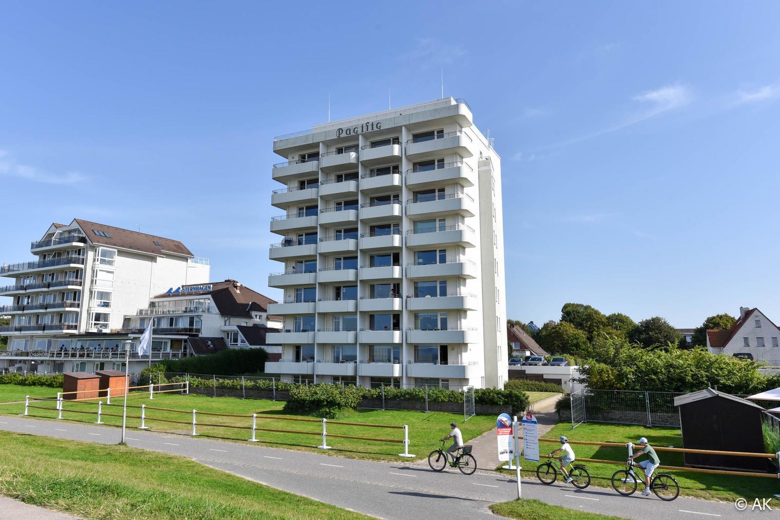Hochhaus mit Balkonen an Strandpromenade, Fahrradfahrer vorbei