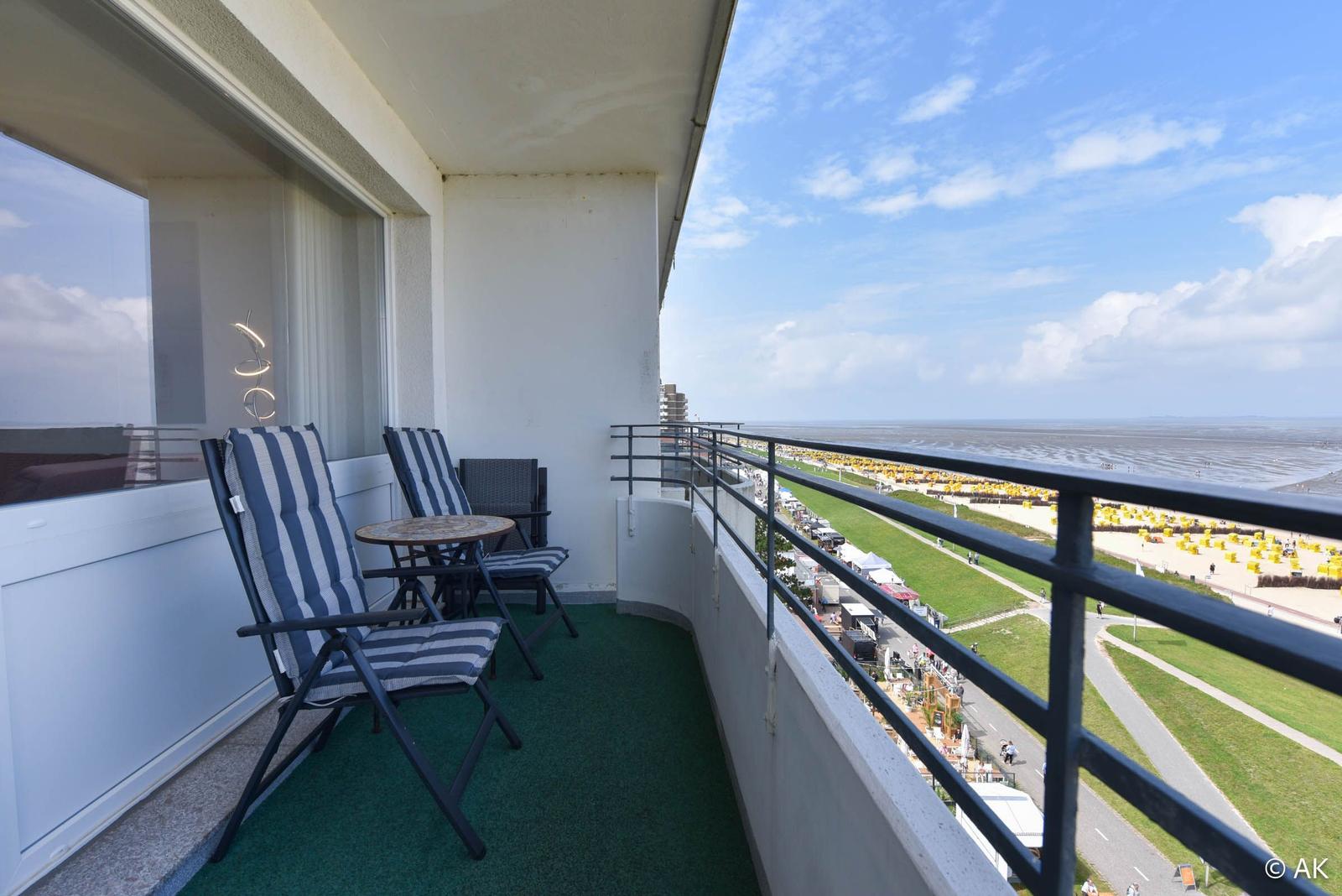 Balkon mit Sitzgelegenheiten und Meerblick auf Strand und Grünfläche.