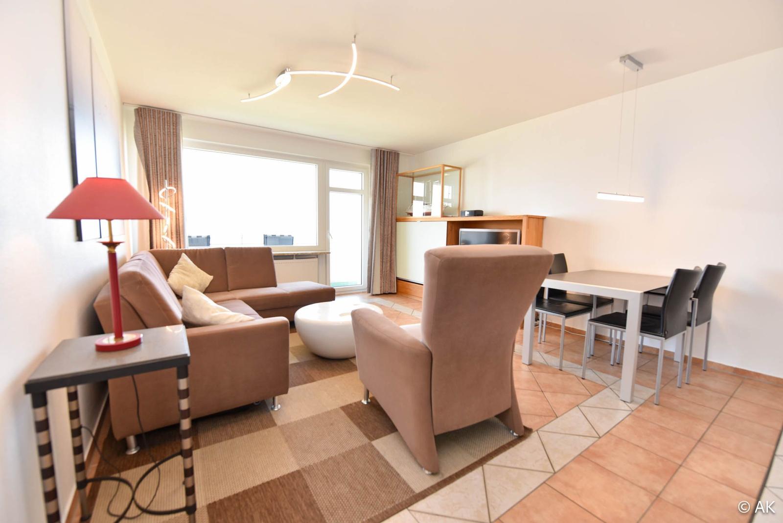 Wohn- und Essbereich mit Sofa, Sessel, Tisch und Fenster.