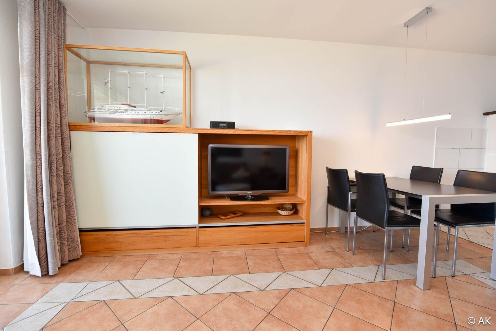 Wohn- und Essbereich mit Fernseher, Tisch und Stühlen sowie Modell Schiff.