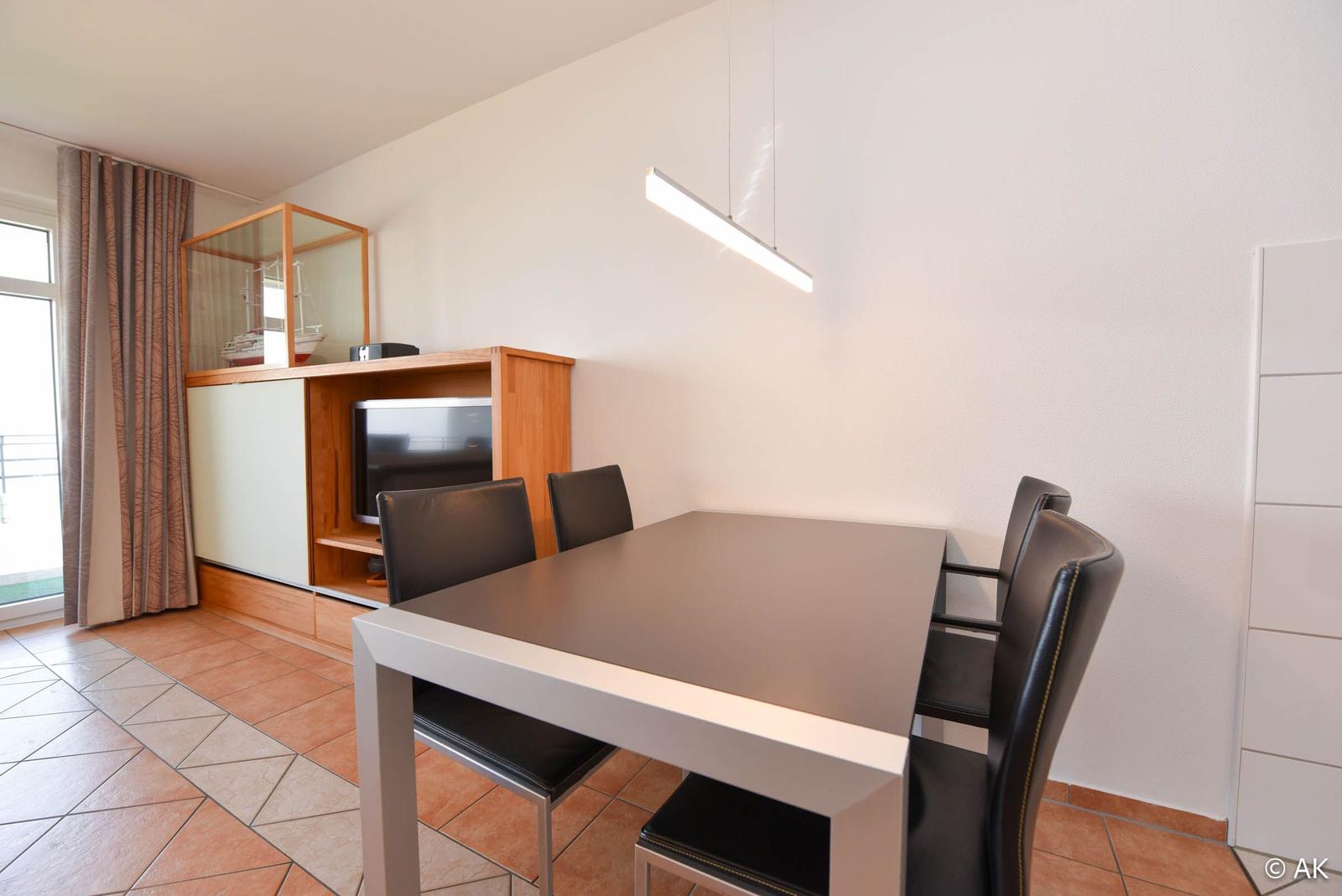 Esstisch mit vier Stühlen, Fernseher und Blick auf Balkon.