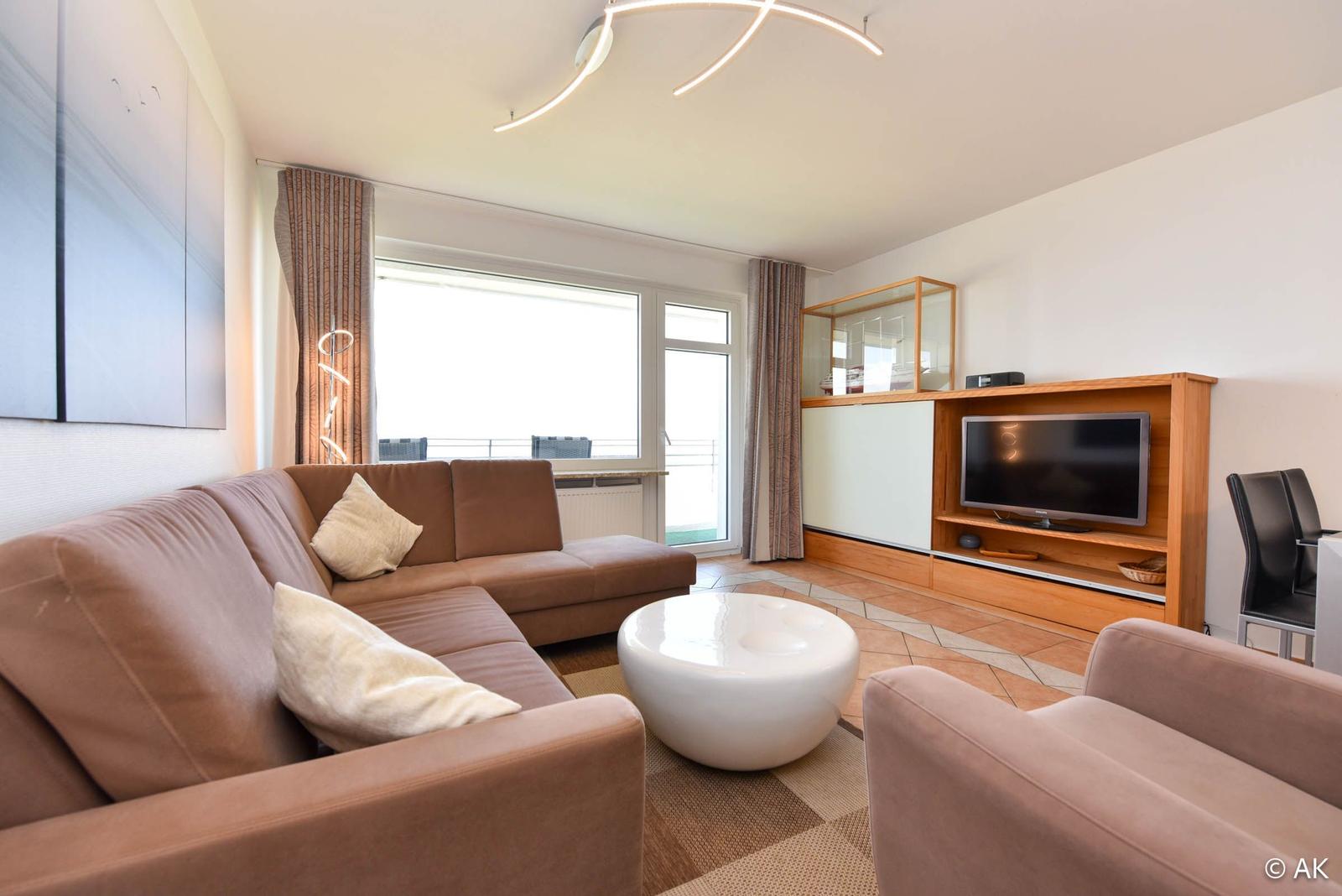 Wohnzimmer mit Sofa, Couchtisch und Fernseher. Fenster mit Blick auf Balkon.