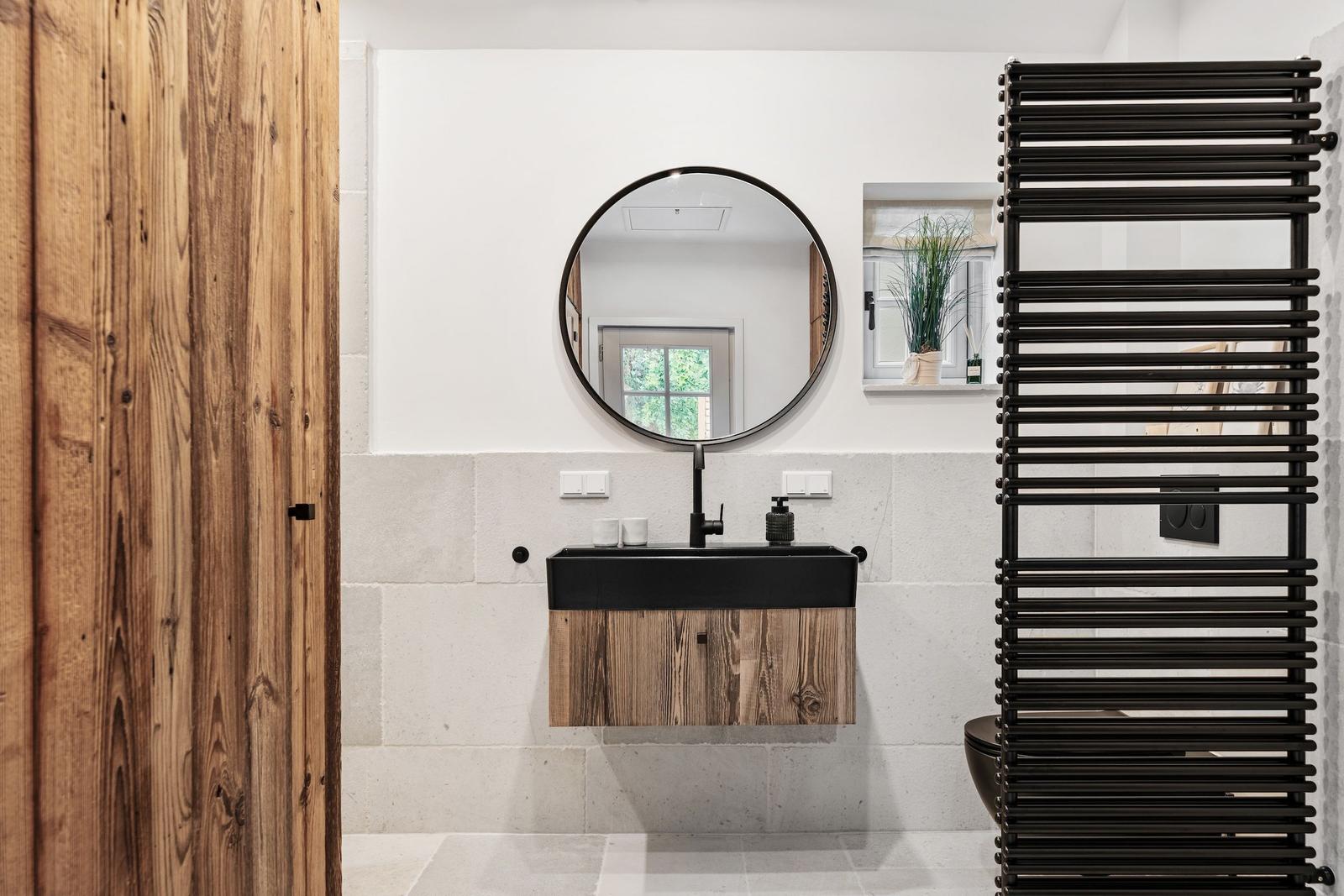 Badezimmer mit Holztür, runden Spiegel und schwarzer Waschbeckenkonsole.