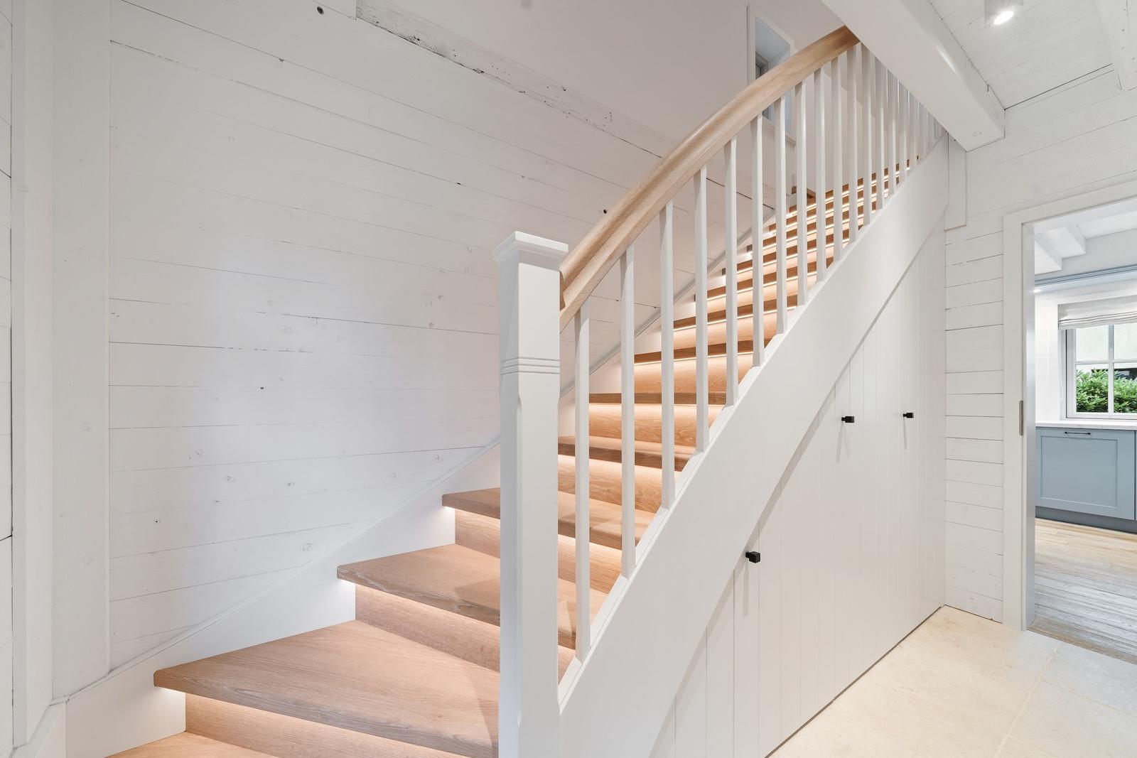 Holzgetreppe mit weißem Geländer führt zur oberen Etage.