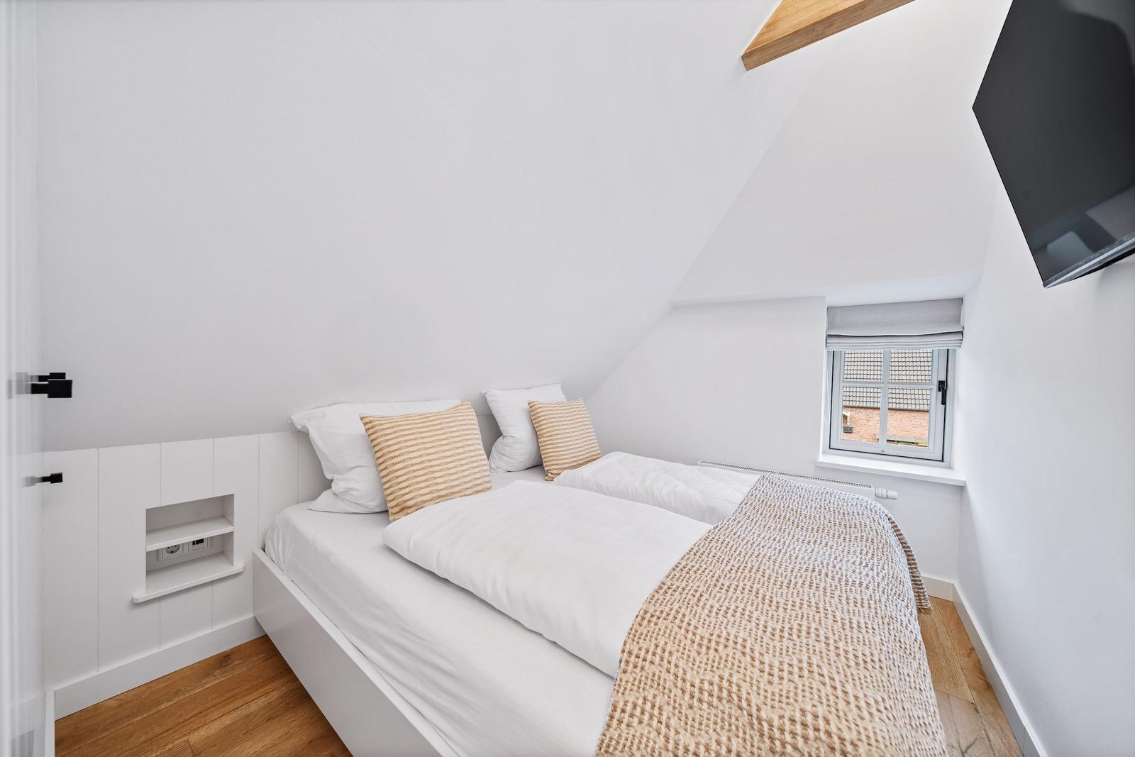 Schlafzimmer mit Doppelbett, Fenster und Fernseher an der Wand.