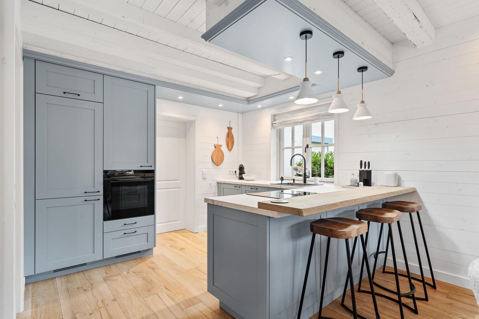Küche mit grauen Schränken, Holzoberfläche und Barhocker.