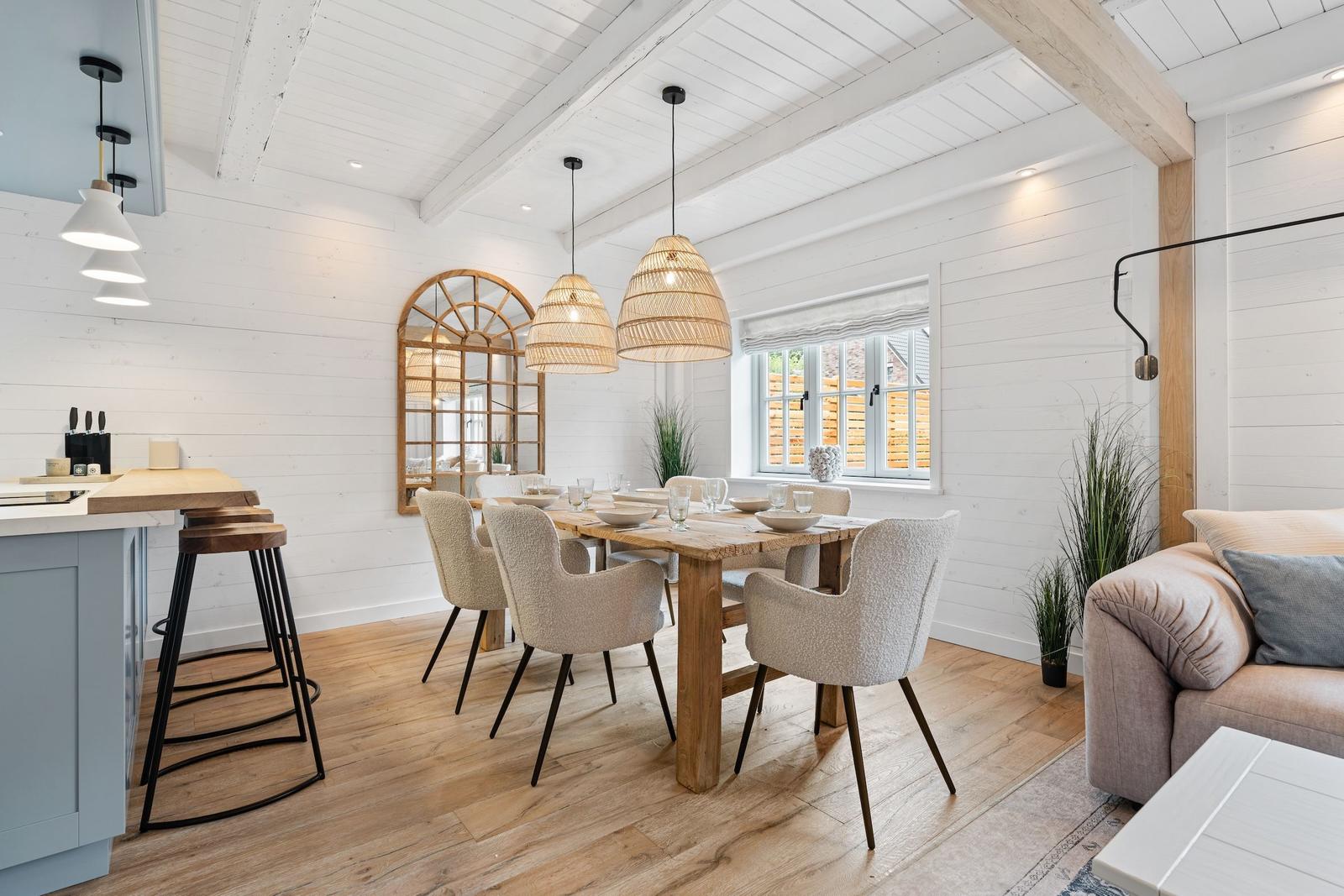 Essbereich mit Holztisch, Stühlen und Fenster. Küche mit Barhocker. Wohnbereich mit Sofa.