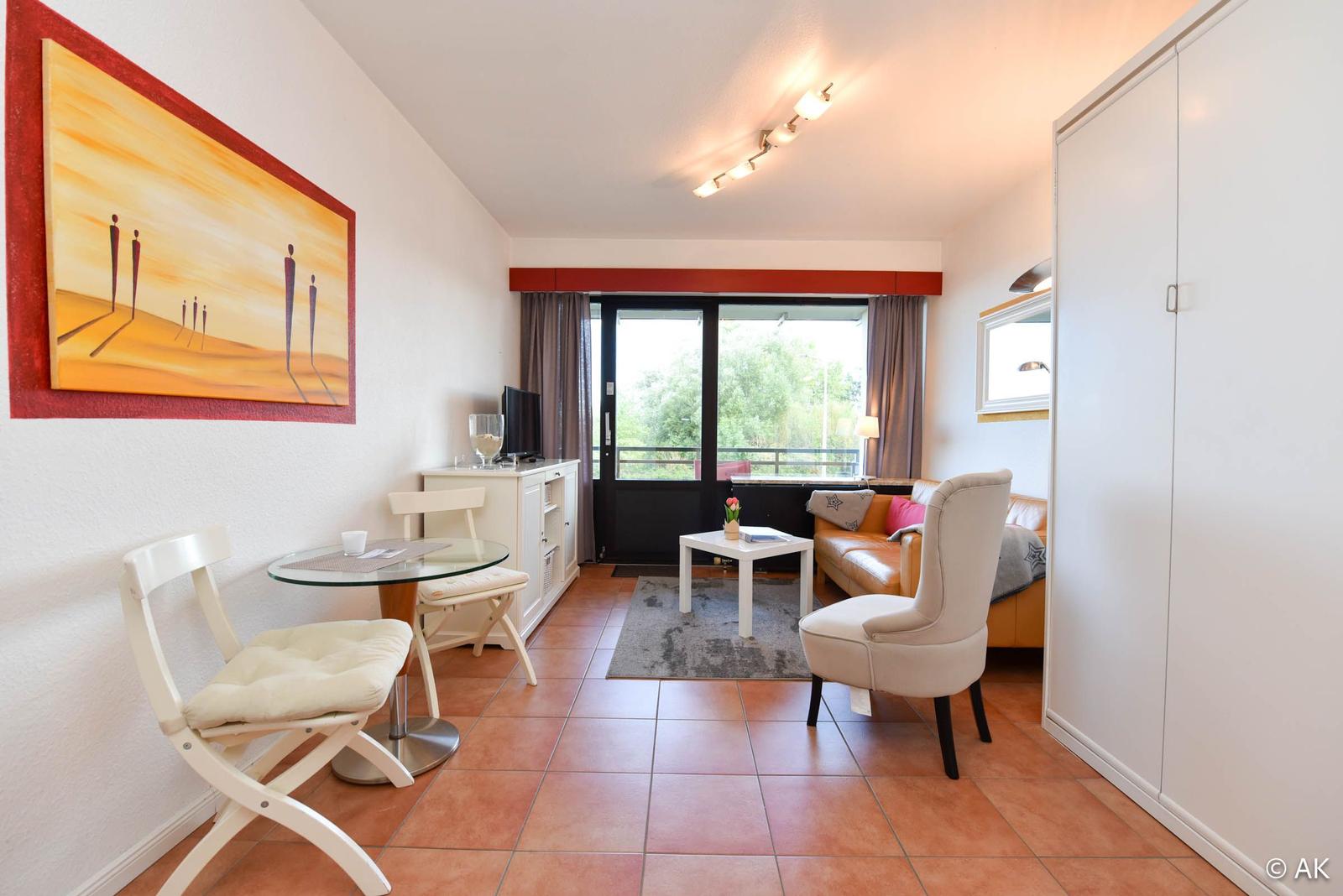 Wohnbereich mit Sofa, Sitzgruppe und Essplatz. Große Fensterfront mit Blick auf Balkon.