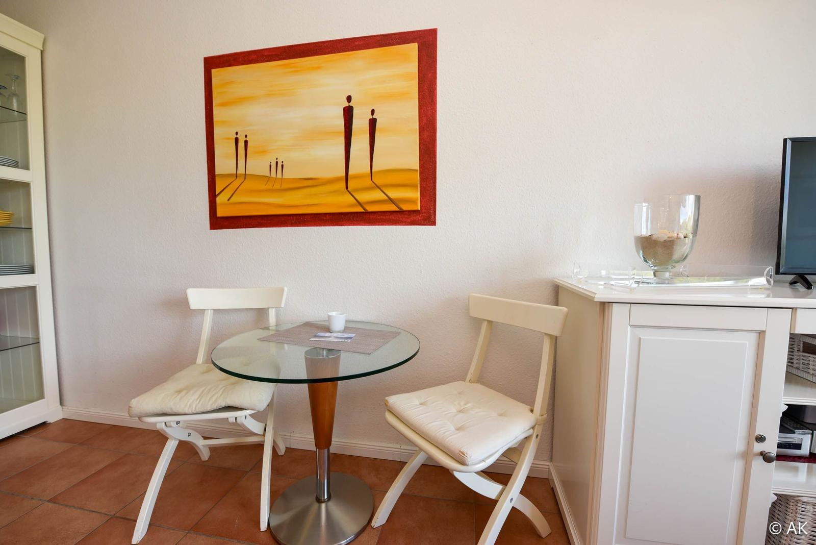 Kleiner Essbereich mit Tisch, zwei Stühlen und Wandbild.