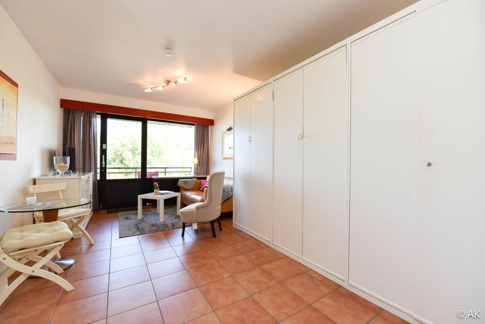 Wohnzimmer mit Schlafbereich, Terrasse und weißen Schränken.