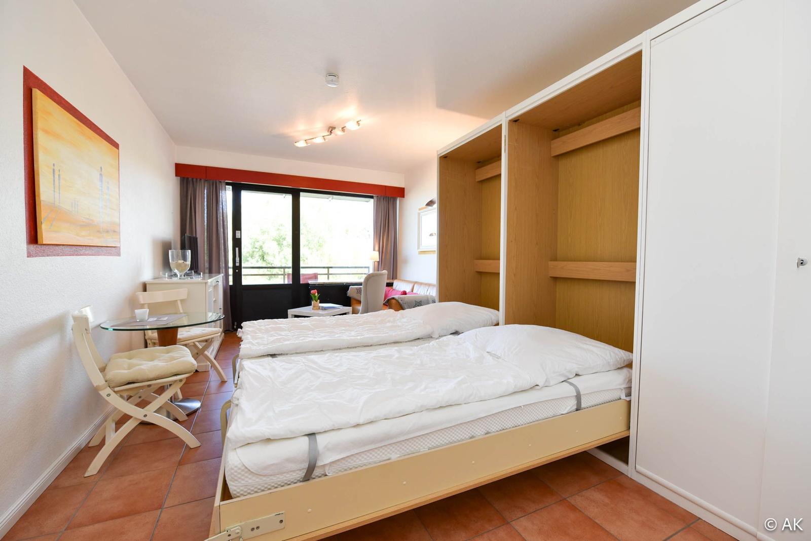 Schlafzimmer mit Bett, Kleiderschrank und Sitzbereich. Fenster mit Blick nach draußen.