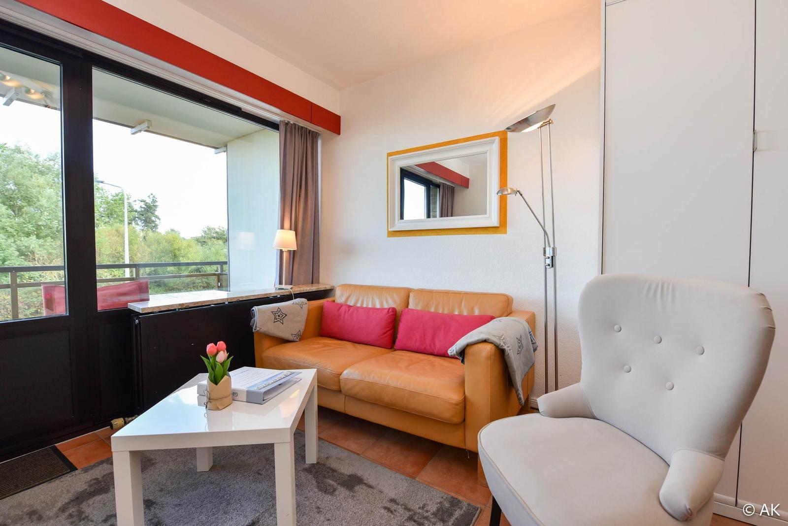 Wohnzimmer mit Sofa, Sessel und Balkonansicht.