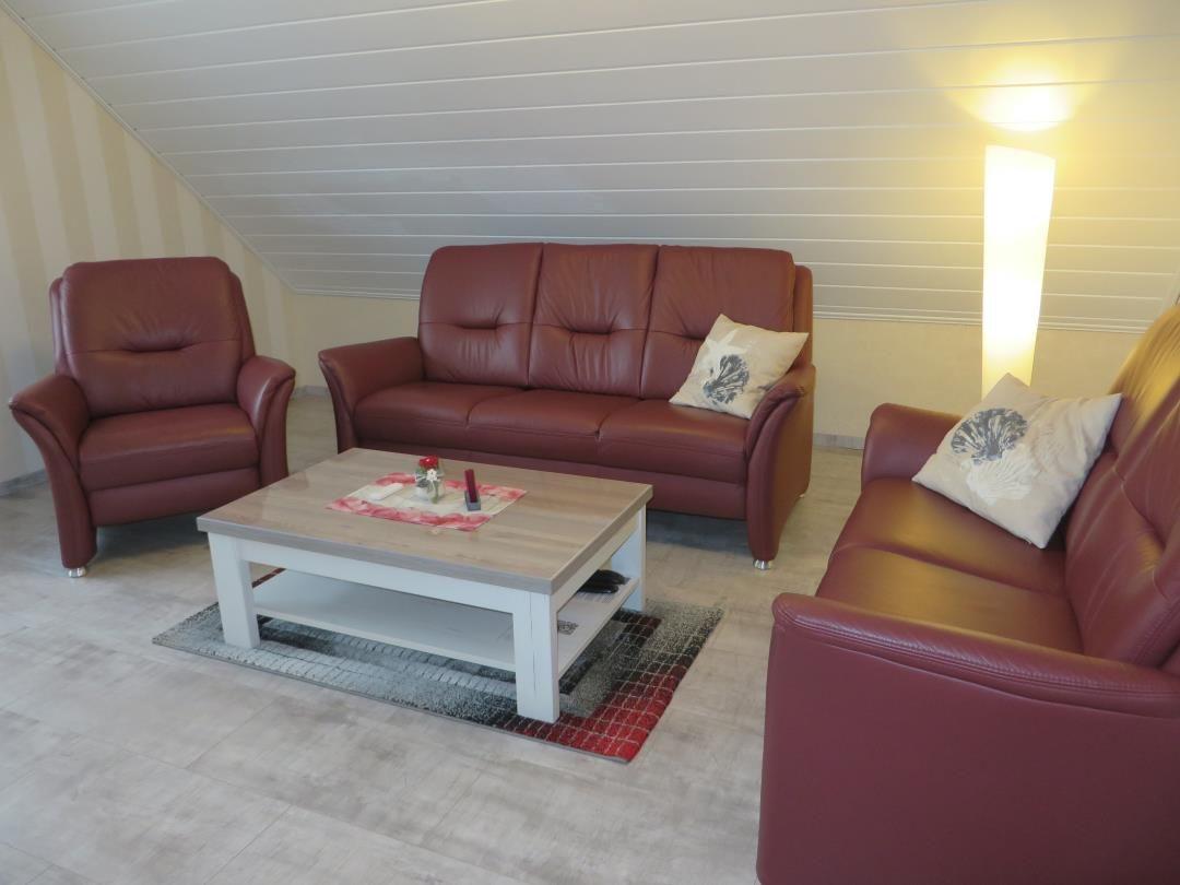 Wohnzimmer mit rotem Ledersofa, Sessel und Tisch.