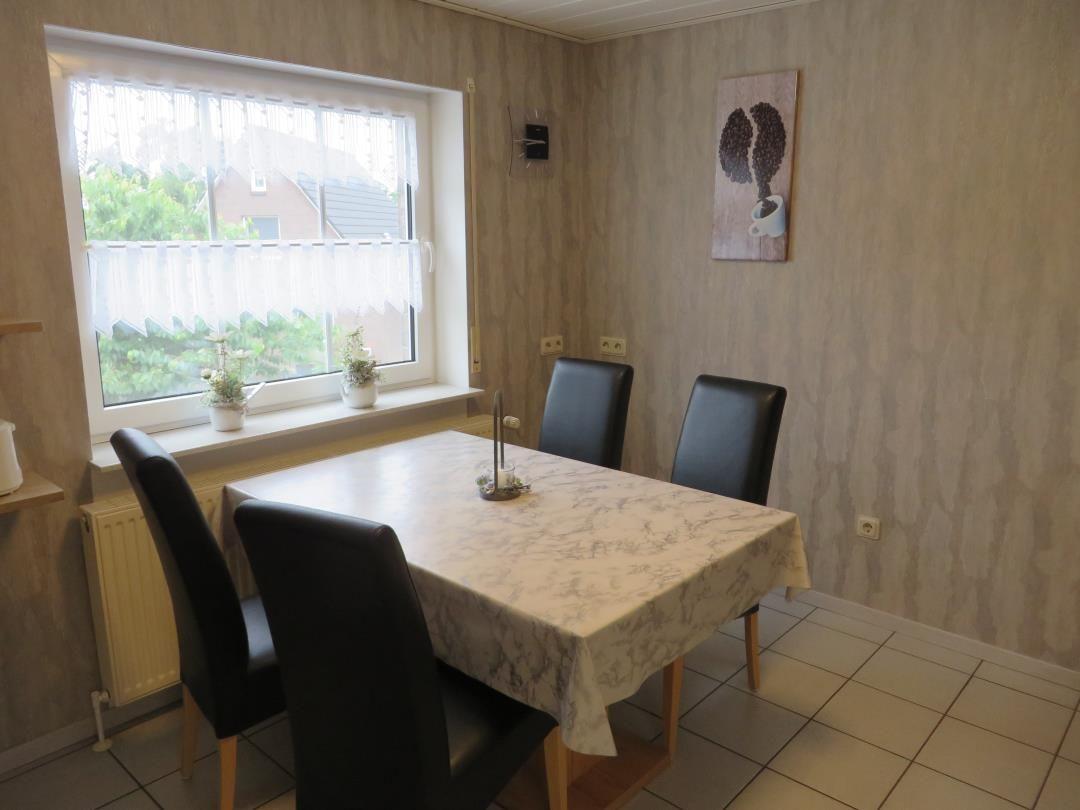 Esszimmer mit Tisch, vier Stühlen und Fenster. Wandbild und Blumen auf dem Fensterbrett.