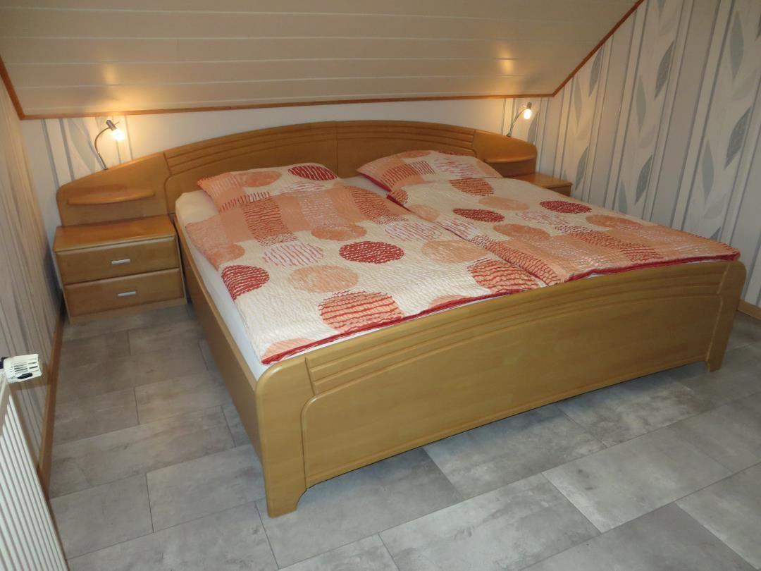 Schlafzimmer mit Doppelbett, Holzgestell und gemustertem Bettbezug.