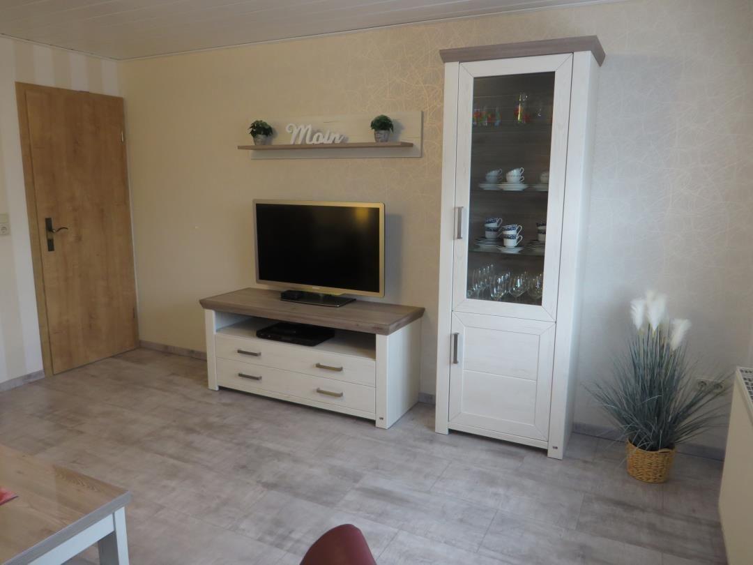 Wohnzimmer mit TV, Schrank und Pflanze.