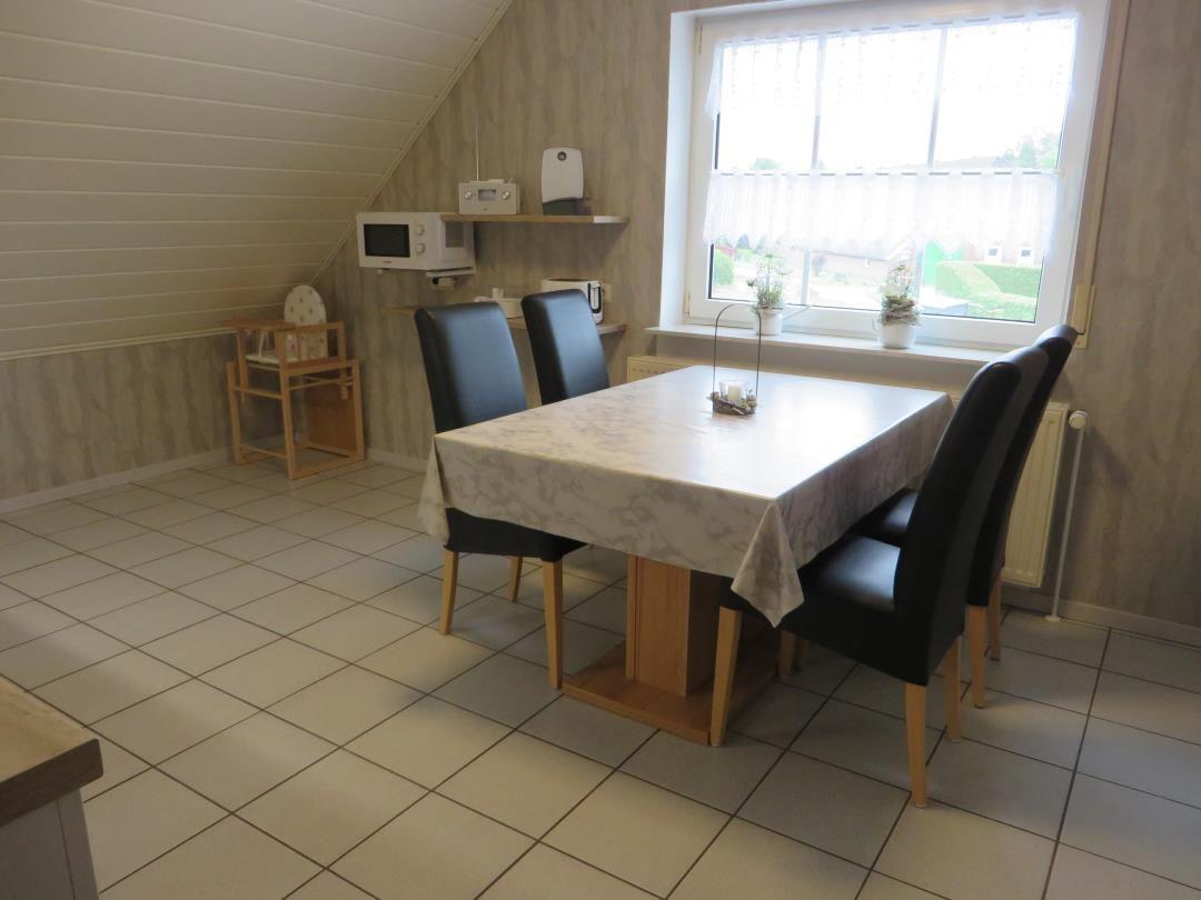 Esszimmer mit Tisch, Stühlen und Fenster. Mikrowelle und Kindersitz sind vorhanden.