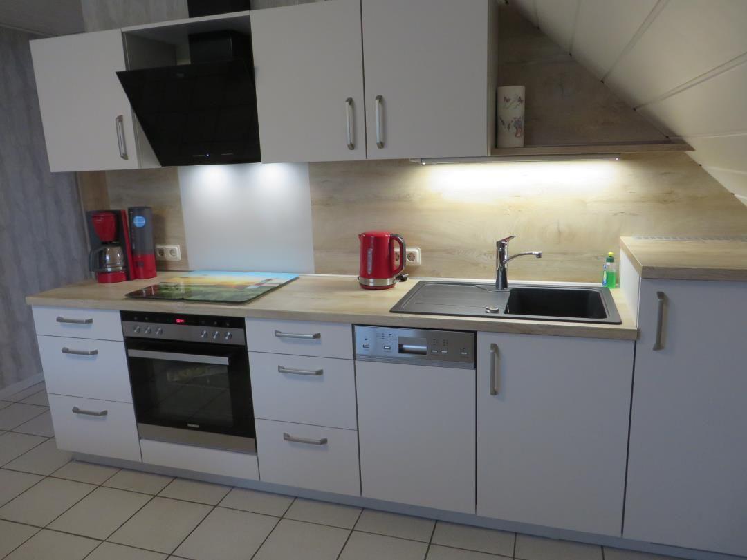 Küche mit weißen Schränken, Edelstahlspüle und rotem Wasserkocher.