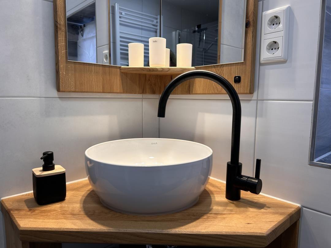 Waschbecken mit schwarzer Armatur auf Holzunterlage, Spiegel mit Holzrahmen und Kerzen.