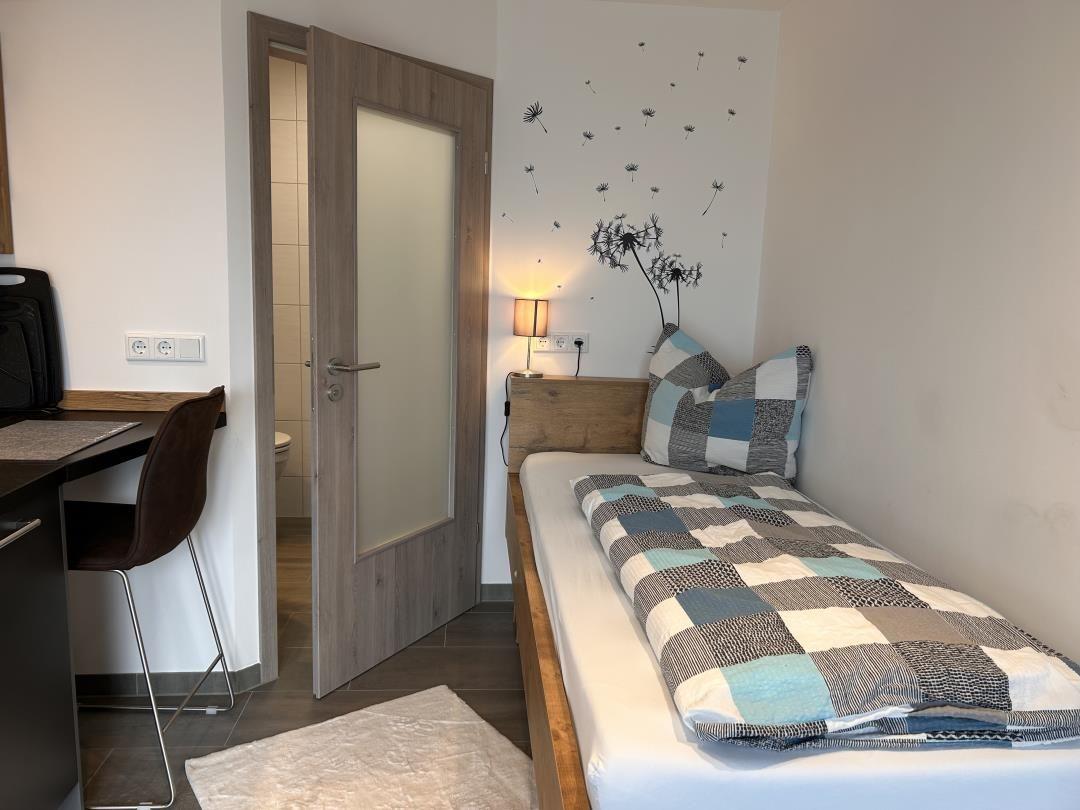 Schlafzimmer mit Bett, Schreibtisch und Tür zum Bad.