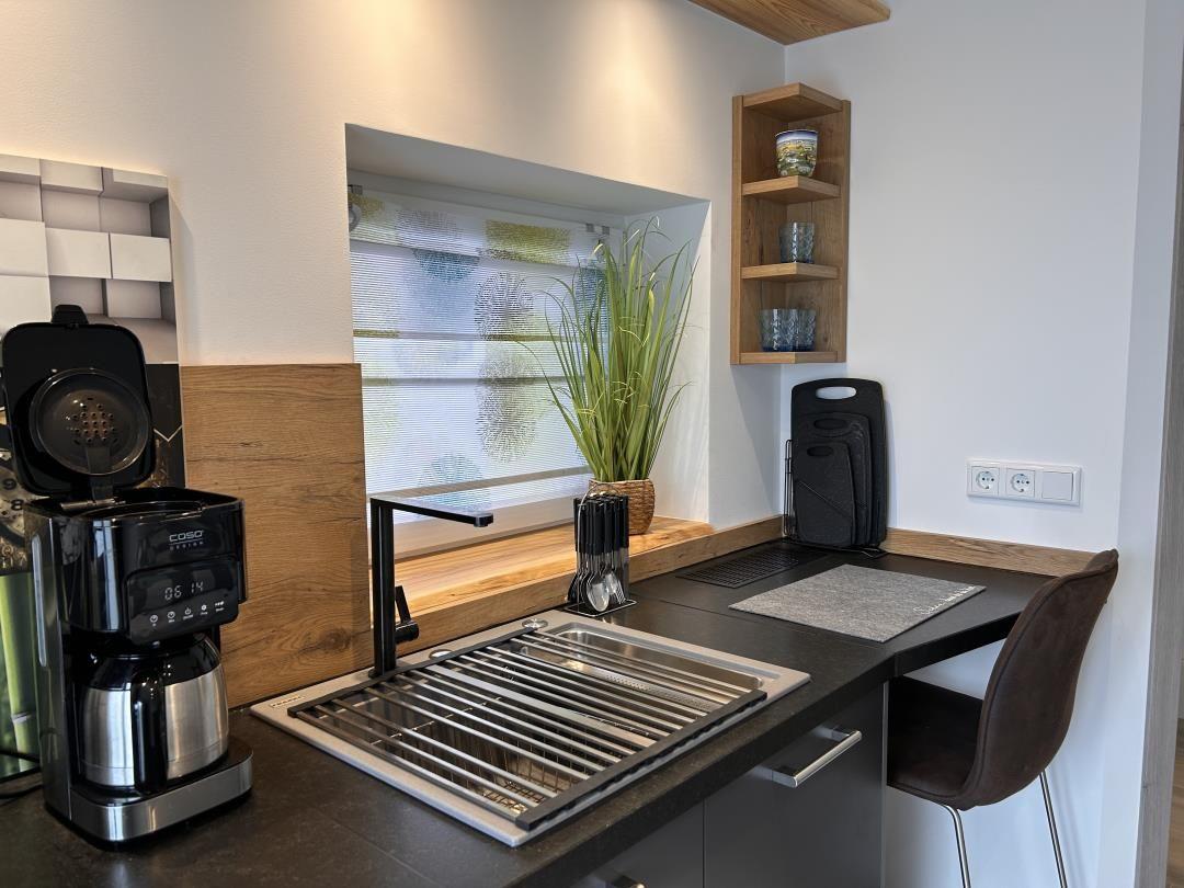 Küche mit Spüle, Kaffeemaschine und Pflanze an Fenster