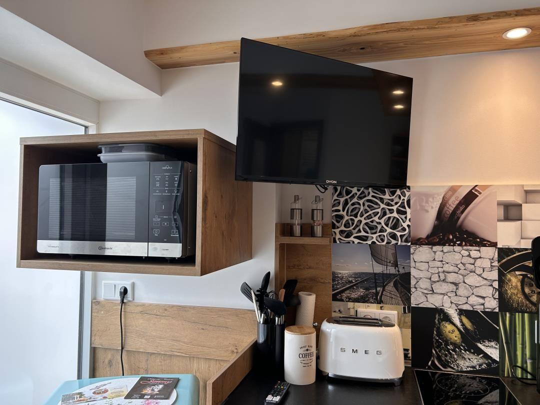 Küche mit Mikrowelle, Toaster und Fernseher an der Wand.