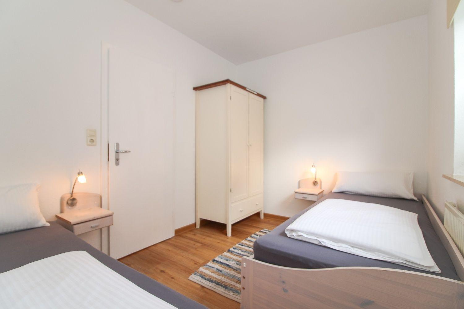 Zimmer mit zwei Betten, Kleiderschrank und Nachttischen mit Lampen.