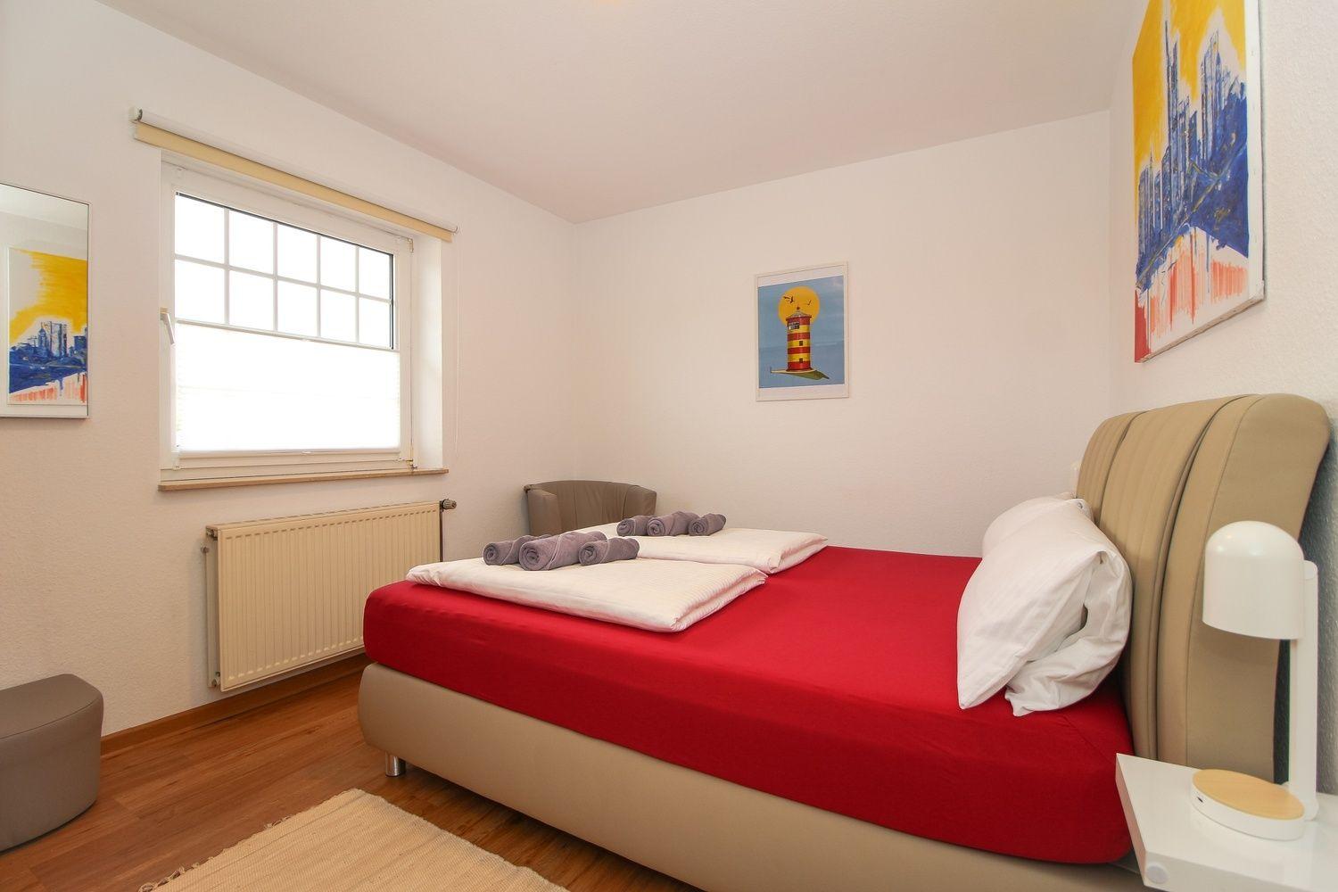 Schlafzimmer mit Bett, Fenster und Wandbildern.