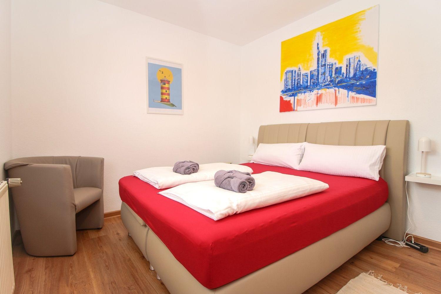 Schlafzimmer mit Bett, Sessel und Wandbildern.