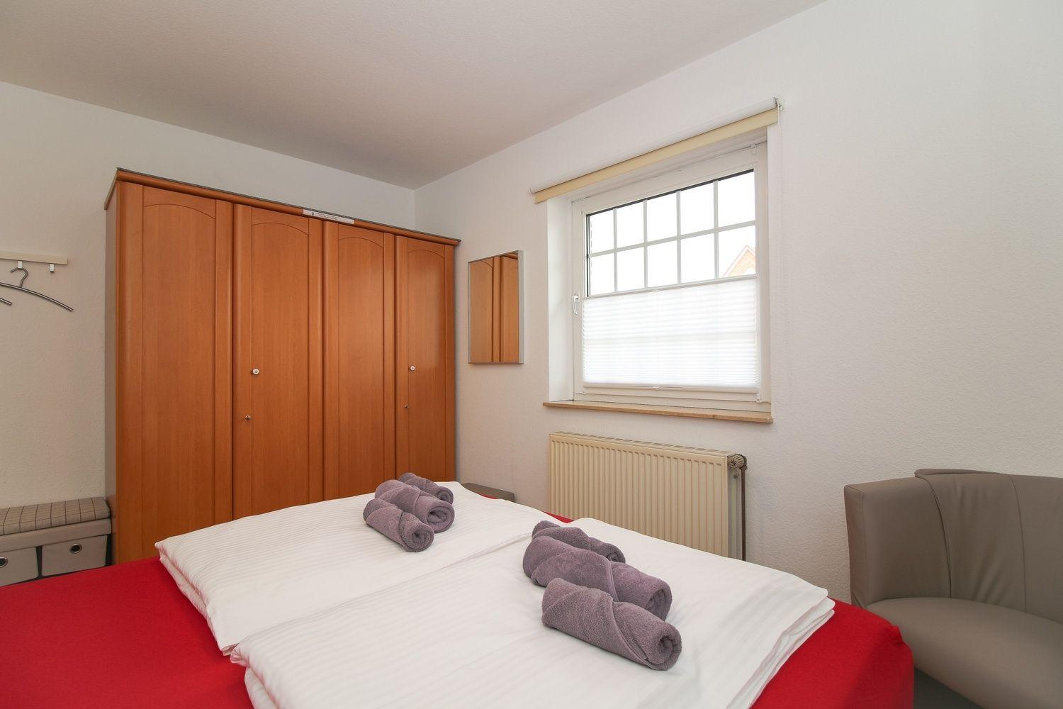 Schlafzimmer mit Bett, Kleiderschrank, Fenster und Sitzgelegenheit.