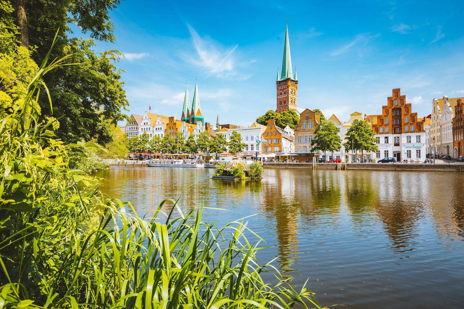 Hafenstadt mit historischen Gebäuden und grüner Ufervegetation unter blauem Himmel.